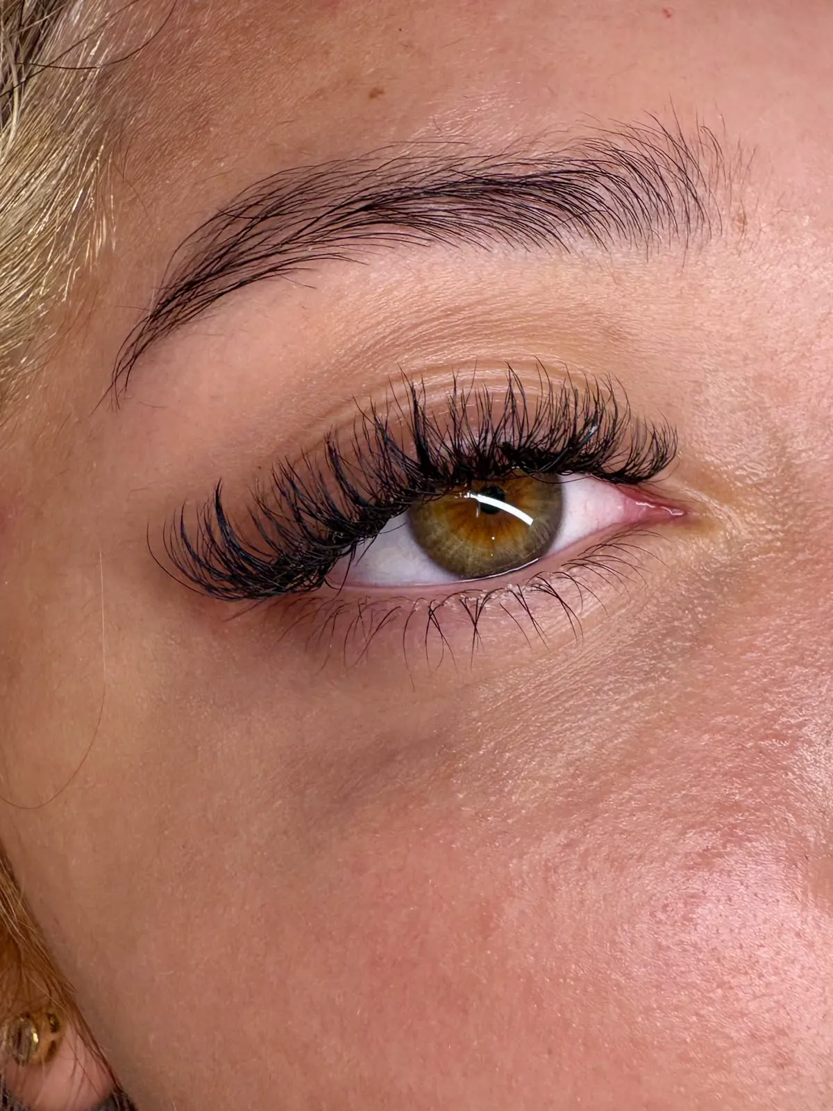 Close de um olho castanho com extensão de cílios curvados.